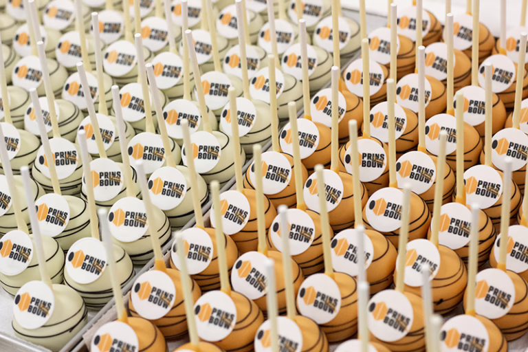 Branded oranje en witte cake pops met zwarte details en logo, in huisstijl kleuren