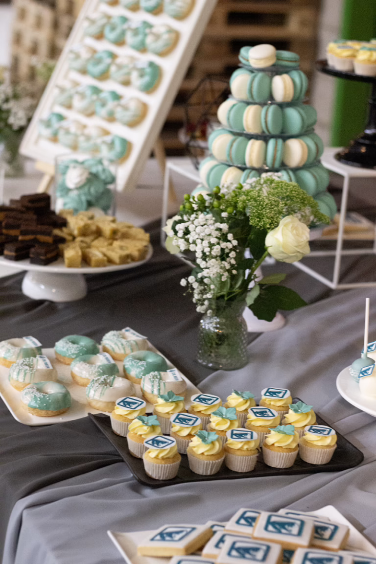 Zakelijke sweet table in zwart-turquoise- branding kleuren. Op veel gebakjes logo decoratie. Donut wall, macaron toren, branded cupcakes - prachtig gepresenteerd.