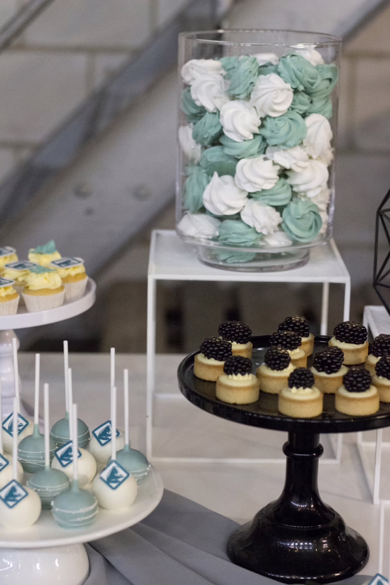 Zakelijke sweet table in zwart-turquoise- branding kleuren. Op veel gebakjes logo decoratie. Donut wall, macaron toren, branded cupcakes - prachtig gepresenteerd.