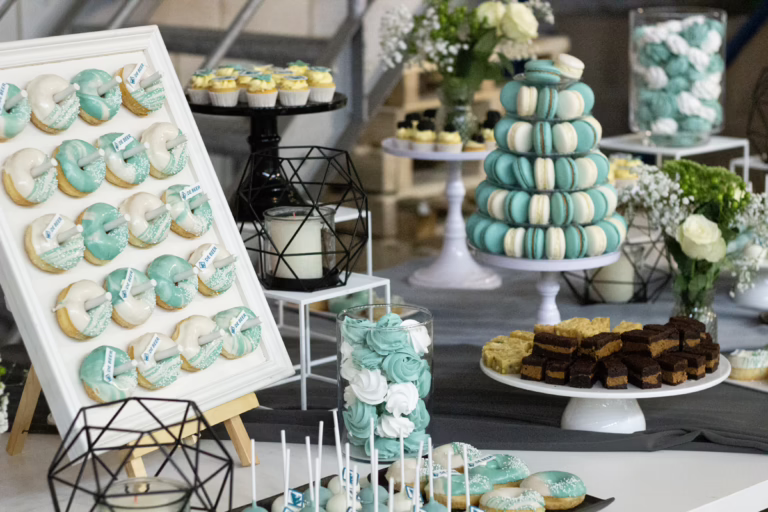 Zakelijke sweet table in zwart-turquoise- branding kleuren. Op veel gebakjes logo decoratie. Donut wall, macaron toren, branded cupcakes - prachtig gepresenteerd.
