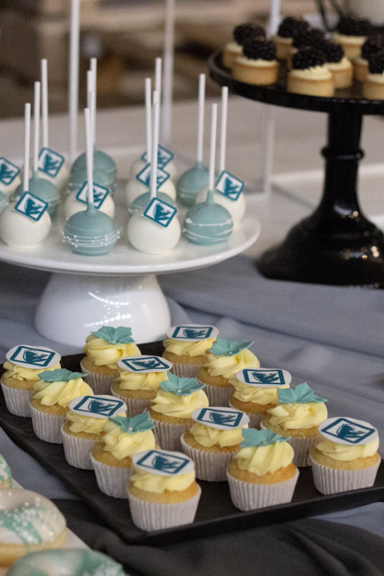 Zakelijke sweet table in zwart-turquoise- branding kleuren. Op veel gebakjes logo decoratie. Donut wall, macaron toren, branded cupcakes - prachtig gepresenteerd.